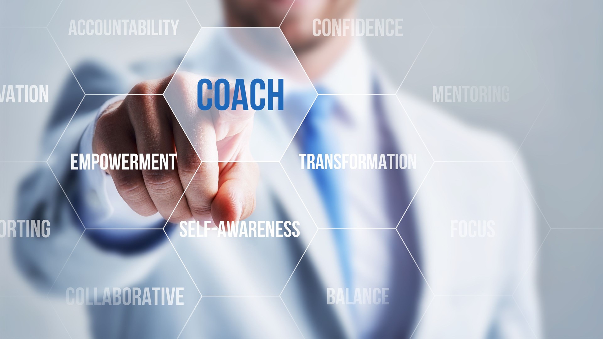 Businessperson pointing to the word coach surrounded by empowerment and transformation terms.